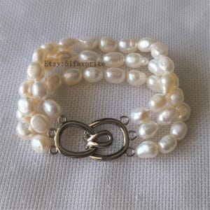 May include: A three-strand bracelet with off-white, irregularly shaped pearls. The bracelet is fastened with a silver-toned clasp. The Etsy shop name "Etsy: 51favorite" is visible in the image.
