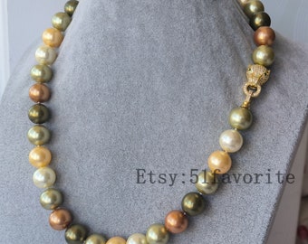 May include: A multi-colored pearl necklace with a gold clasp featuring a lion head design. The necklace is made of large, round pearls in shades of green, gold, and brown. The pearls are strung on a gold chain and the clasp is secured with a small gold loop. The necklace is displayed on a gray background. Etsy: 5lfavorite