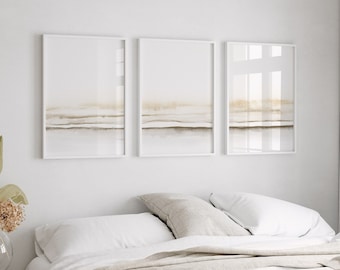 May include: A white bed with a beige linen blanket and three white pillows. Three framed abstract paintings with a beige and brown color scheme hang on the wall above the bed.