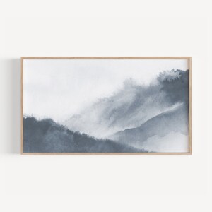 Pode incluir: Uma pintura de aquarela emoldurada de uma paisagem montanhosa nebulosa em tons de azul e cinza.