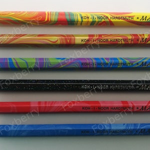 May include: Six different colored pencils with the brand name "KOH-I-NOOR HARDTMUTH MAGIC" printed on each. The pencils are arranged vertically from top to bottom: original, fire, tropical, neon, America red, and America blue.