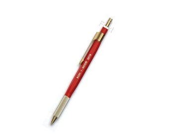 May include: A red mechanical pencil with a silver tip and a gold-colored clip. The pencil is labeled "KOH-I-NOOR 5219".