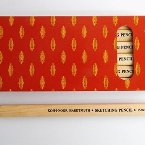 May include: A box of Koh-I-Noor Hardtmuth sketching pencils in a red and gold patterned box. The box has a window showing the pencils. The pencils are labelled "G PENCIL" and "PENCIL". A single wooden pencil is shown below the box. The pencil is labelled "KOH-I-NOOR HARDTMUTH SKETCHING PENCIL 1538/2B".
