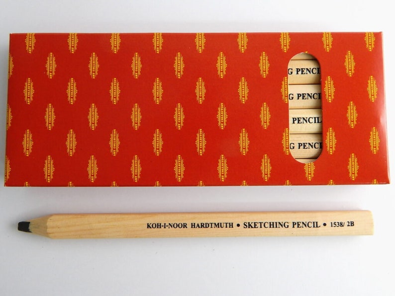 May include: A box of Koh-I-Noor Hardtmuth sketching pencils in a red and gold patterned box. The box has a window showing the pencils. The pencils are labelled "G PENCIL" and "PENCIL". A single wooden pencil is shown below the box. The pencil is labelled "KOH-I-NOOR HARDTMUTH SKETCHING PENCIL 1538/2B".