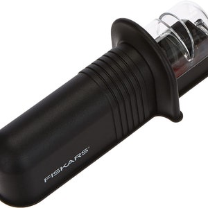 Peut inclure: Aiguiseur à couteaux en plastique noir avec un dessus en plastique transparent et un mécanisme d'affûtage rouge et argenté. L'aiguiseur a une poignée texturée et le mot "FISKARS" imprimé sur le côté.