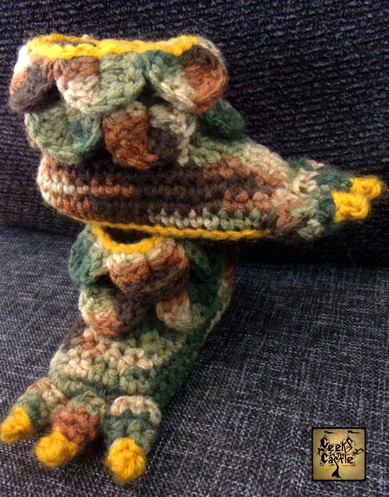 May include: Crocheted slippers with a camouflage pattern and yellow trim. The slippers have a pointed toe and a textured design.