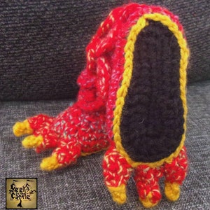 May include: Red and yellow crocheted slipper with a black sole and three toes. The slipper is made of yarn and has a textured surface.
