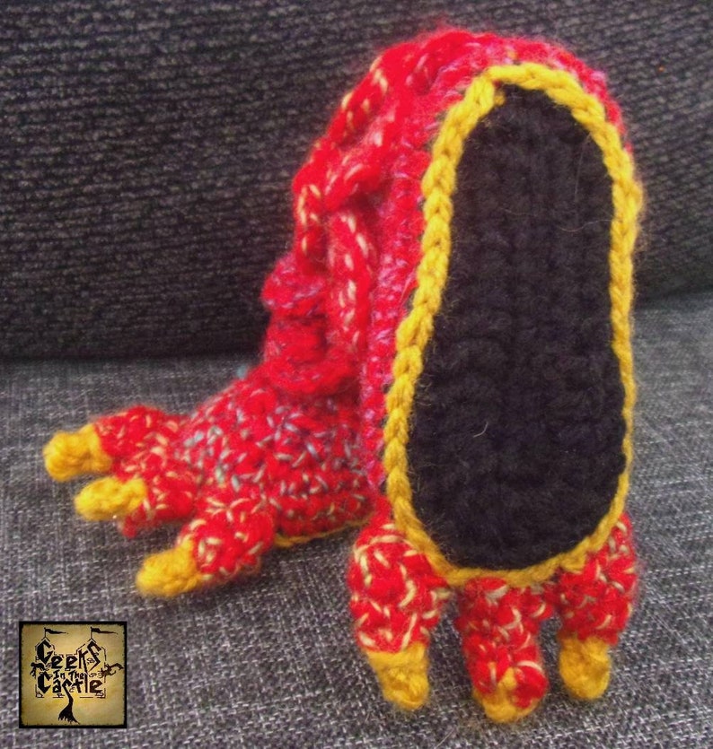 May include: Red and yellow crocheted slipper with a black sole and three toes. The slipper is made of yarn and has a textured surface.