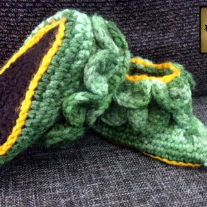 May include: Green and yellow crocheted slippers shaped like a dragon's foot. The slippers have a black felt lining and yellow toes.