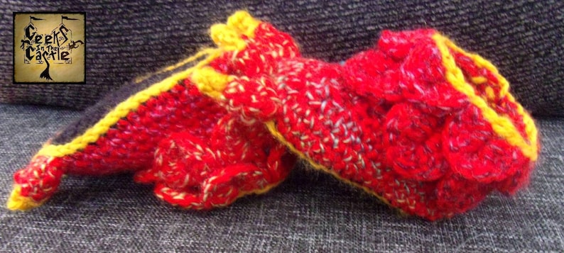 May include: A pair of red and yellow crocheted slippers with a textured design. The slippers are on a gray fabric surface.