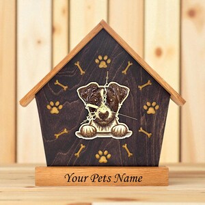 May include: Wooden dog house-shaped clock with a brown and white dog illustration. The clock features paw prints and bone accents. The base of the clock reads "Your Pets Name".