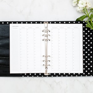 May include: A black and white polka dot planner with a silver ring binder. The planner is open to the January page, which has a weekly layout.