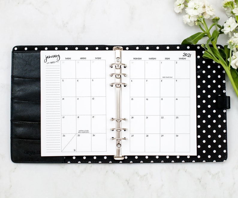 Op de afbeelding: Een zwart-witte stippenplanner met een zilveren ringband. De planner is open voor januari 2021 en heeft een witte achtergrond met zwarte tekst. De planner ligt op een wit marmeren oppervlak.