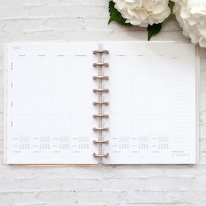 May include: A white weekly planner with a grid layout for tracking meals, snacks, water intake, sleep, and workouts. The planner has a section for notes and a weekly rating system.