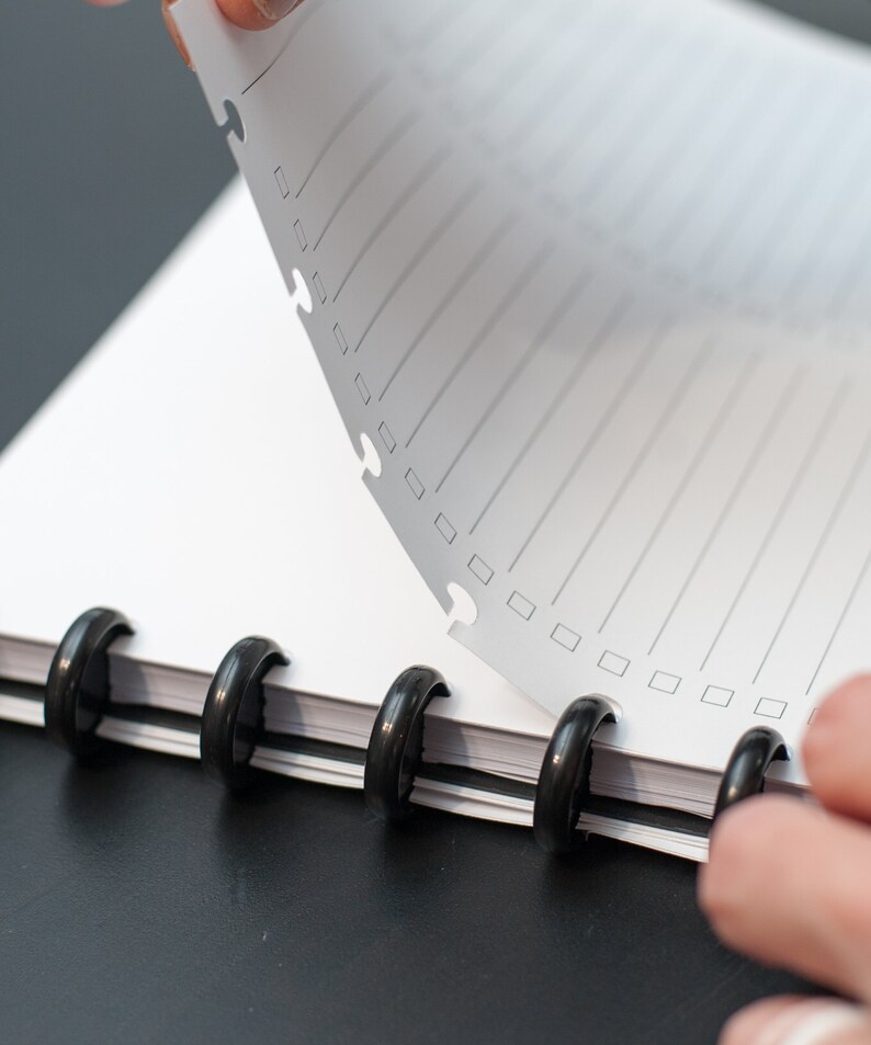 May include: A white notebook with black rings and lined pages. The top page is being turned over to reveal the next page.