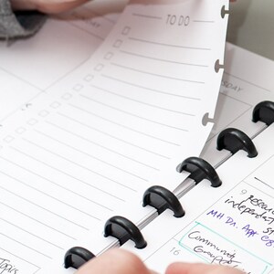 May include: A close-up of a black and silver ring binder with a white page turned to reveal a to-do list. The page has a perforated edge and is labeled "TO DO".
