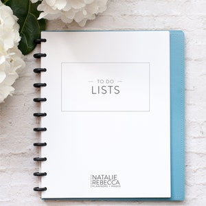 May include: A white planner with a blue cover and a black coil binding. The cover has the text "TO DO LISTS" in black text. The bottom of the cover has the text "NATALIE REBECCA PLANNERS + PAGES" in black text.