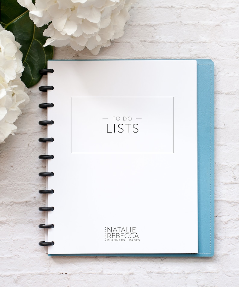 May include: A white planner with a blue cover and a black coil binding. The cover has the text "TO DO LISTS" in black text. The bottom of the cover has the text "NATALIE REBECCA PLANNERS + PAGES" in black text.