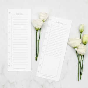 May include: Two white printable to-do list cards with a black "TO DO" title and a dotted line for checking off tasks. The cards are on a white marble surface with white flowers.