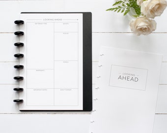 May include: A white planner with a black cover and a black ring binder. The planner has a section for "Looking Ahead" with categories for "Get Ready For", "Focus", "Goals", "Birthdays", "Important Dates", and "Don't Forget". The planner also has a title page with the text "Looking Ahead" and the name "Natalie Rebecca Planners + Pages".