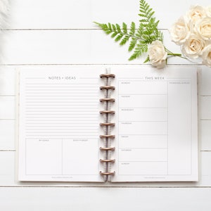 May include: An open planner with a white background and gold rings. The left page has the words "NOTES + IDEAS" at the top and sections for "MY GOALS" and "DON'T FORGET". The right page has the words "THIS WEEK" at the top and a weekly calendar with the days of the week listed. The words "THINKING AHEAD" are at the top of the right column.