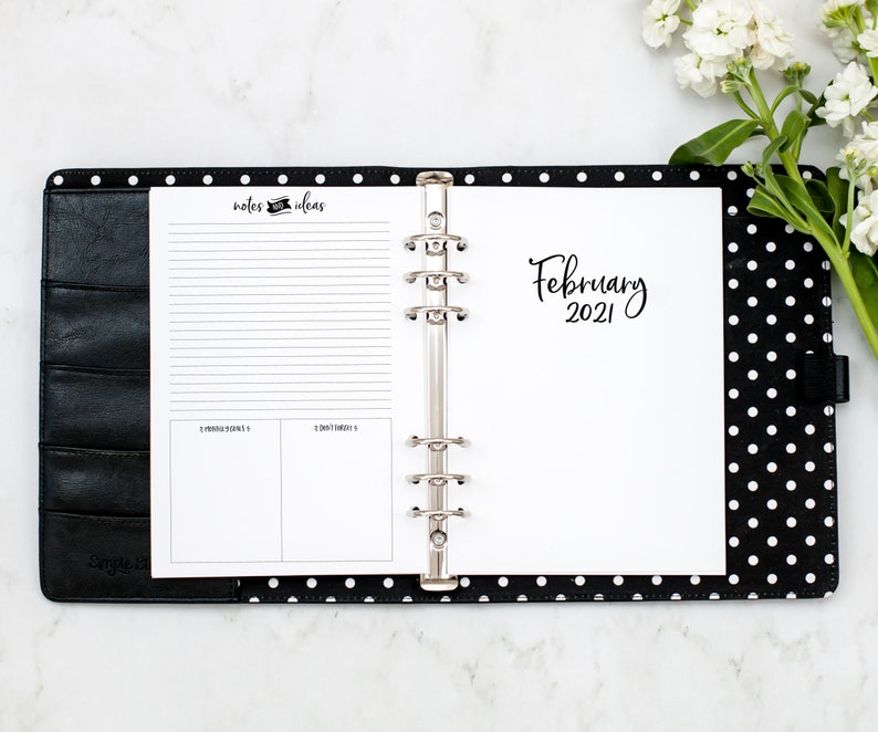 Op de afbeelding: Een zwarte en witte stippenbinder met een witte pagina open voor februari 2021. De linkerpagina heeft een sectie voor notities en idee&euml;n met gestreept papier en twee lege vakjes.