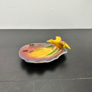 Puede incluir: Un plato decorativo de cerámica con una figura de pato amarillo sobre una colorida escena de estanque. El plato tiene una vibrante paleta de colores amarillo, naranja, rojo y verde, con un acabado brillante. Un artículo decorativo único.
