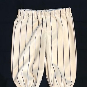 May include: White baseball pants with navy blue vertical stripes. The pants have an elastic waistband and gathered cuffs at the ankles. The fabric has a slight sheen. The pants are designed for a child.