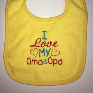 May include: Yellow baby bib with embroidered text that reads "I love my Oma & Opa" with red, blue, and teal thread.
