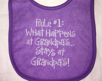 May include: Purple baby bib with white embroidery that reads "Rule #1: What Happens at Grandpa's... Stays at Grandpa's!"