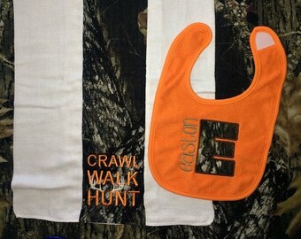 Op de afbeelding: Een witte en camouflage baby spuugdoek met de tekst "crawl walk hunt" erop geborduurd. Een feloranje slab met de tekst "Easton" en een camouflage letter "E" erop geborduurd.