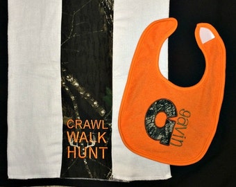 Op de afbeelding: Een witte handdoek met een camouflageprint aan de zijkant. De handdoek heeft de woorden "crawl walk hunt" geborduurd. Een feloranje slab met een camouflageletter "G" en de naam "gavin" geborduurd.