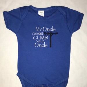 Puede incluir: Un body azul para bebé con el texto "My Uncle can out CLIMB your Uncle" y una silueta negra de un poste de electricidad con líneas eléctricas.