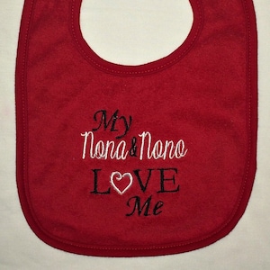 以下が含まれることがあります： 白いハートと「My Nona & Nono LOVE Me」という白黒の刺繍が施された赤いベビーよだれかけ