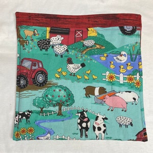 Può includere: Un tessuto verde con una scena di fattoria che presenta un trattore rosso, un fienile, animali e una staccionata bianca. Il tessuto ha un bordo rosso.