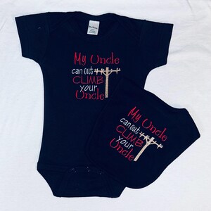 May include: Black baby bodysuit and bib set. The bodysuit and bib have the embroidered phrase "My Uncle can out climb your Uncle" in red and gold thread. The design includes a utility pole.
