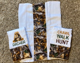 Op de afbeelding: Drie witte spuugdoeken met een camouflageprint. Een doek heeft de letter A en de naam "Archer" geborduurd. Een andere doek heeft de woorden "Crawl Walk Hunt" geborduurd.
