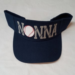May include: A navy blue baseball visor with a white baseball and the word "NONNA" in grey lettering.