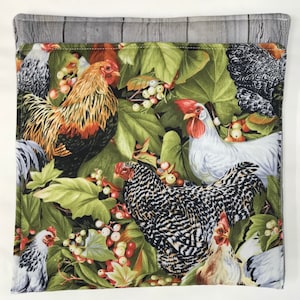 May include: A colorful fabric with a pattern of chickens and roosters in a green leafy setting with red berries. The fabric has a gray border.