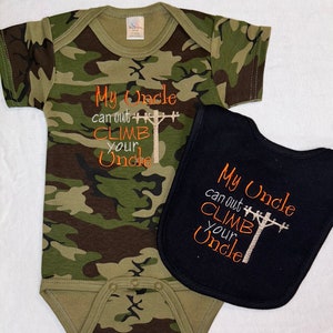 May include: A camouflage-patterned baby onesie and a black bib. The onesie and bib feature the embroidered text "My Uncle can out CLIMB your Uncle" in orange. The onesie has a green and brown camouflage pattern.