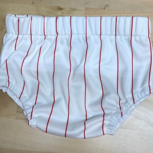 Puede incluir: Bombachos de bebé blancos con rayas verticales rojas. Los bombachos están hechos de una tela suave y elástica.