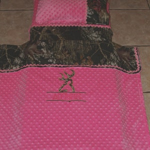 May include: Pink and camo baby blanket with a buck logo and the name "Alayna" embroidered on it.