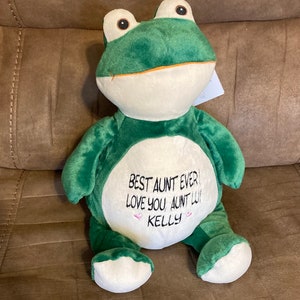 May include: Green plush frog with a white belly. The frog has embroidered text that reads "Best Aunt Ever! Love you, Aunt Lu! Kelly".