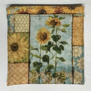 May include: A fabric panel with a patchwork design featuring sunflowers and a blue background. The fabric has a vintage, distressed look.