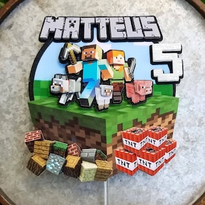 May include: A Minecraft-themed cake topper featuring the name "MATTEUS" and the number "5". The design includes pixelated characters, animals, and blocks, with a green grass and blue sky background. TNT blocks and various building blocks are also included.