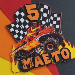 Puede incluir: Adorno de tarta de cumplea&ntilde;os colorido con un dise&ntilde;o de cami&oacute;n monstruo, el nombre "MAETO" y el n&uacute;mero "5". Incluye banderas a cuadros y llamas, con detalles en naranja, negro y blanco.