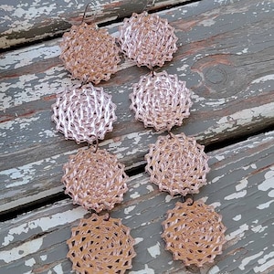 May include: A pair of long, dangling earrings with three circular, layered, rose gold-coloured, openwork designs. The earrings are made of a delicate, intricate pattern.