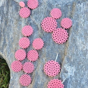 May include: Pink dangle earrings with multiple layered circular designs. The earrings are made of a delicate, intricate pattern.