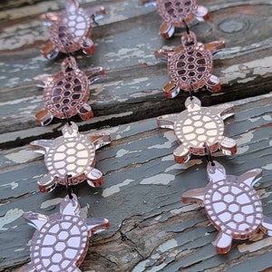 May include: A pair of rose gold earrings featuring a cascade of five turtle charms. Each turtle charm has a detailed shell design.