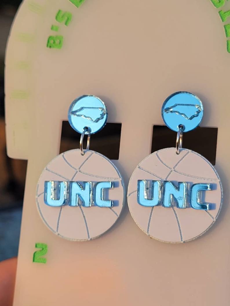 May include: A pair of blue and white basketball-themed earrings with a UNC logo and a North Carolina state outline.